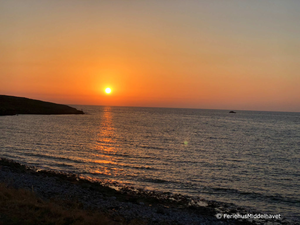 Himmelen er blodrød og gul i det solen går ned ved en odde langs Esentepe kysten, Nord Kypros. Bølger som dovent slår inn mot land.
