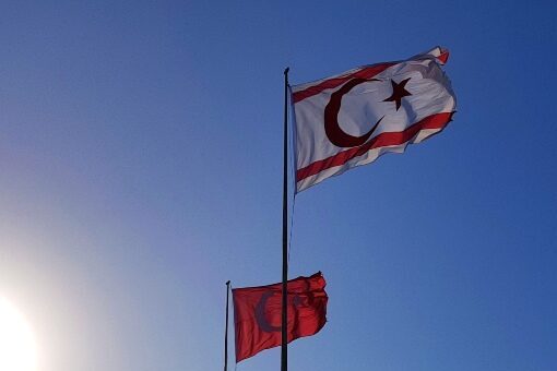 I Generelle fakta Nord Kypros er flagget, hvit med rød halvmåne, stjerne og en rød line på topp og bunnen. På flaggstang mot blå kypriotisk himmel.